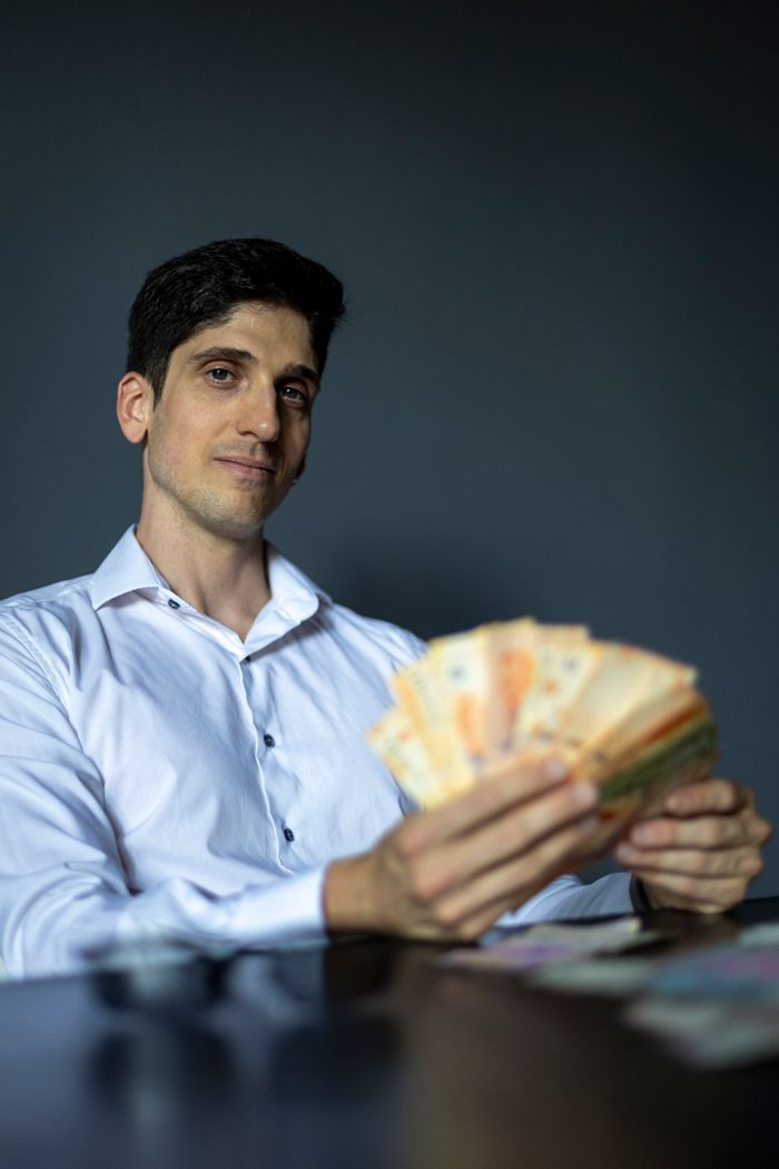 services-04 Businessman in a white shirt holding Argentine pesos with a confident expression indoors.