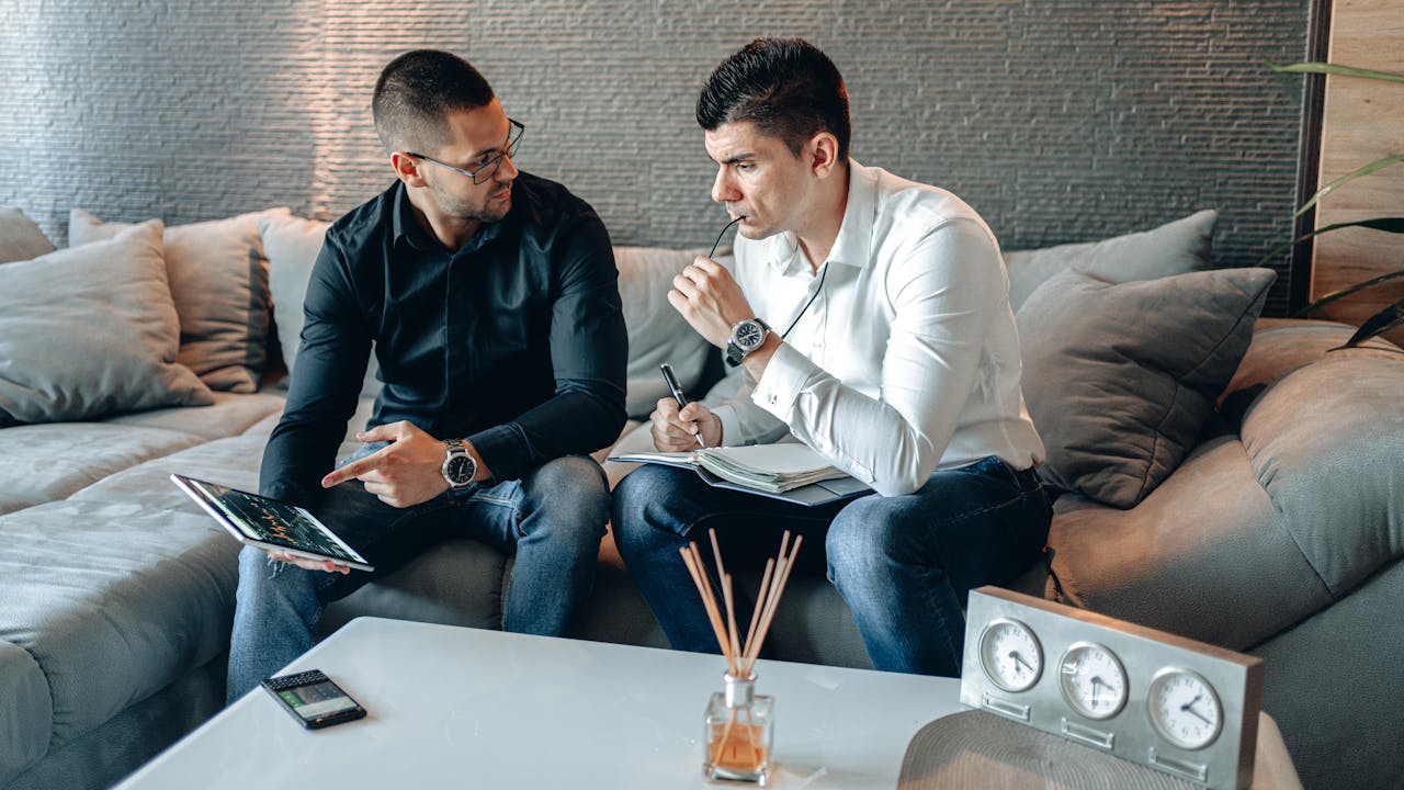 Mastering the First Impression: Your intriguing post title goes here Two businessmen discussing ideas with digital tablet and notepad in a stylish office.