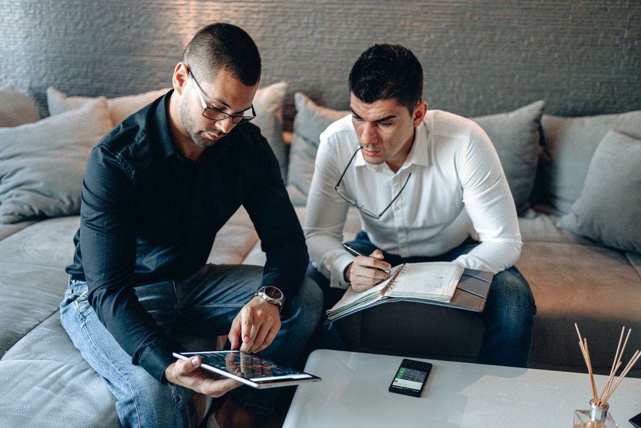 services-01 Two businessmen working together with a tablet and notebook in a contemporary home office space.