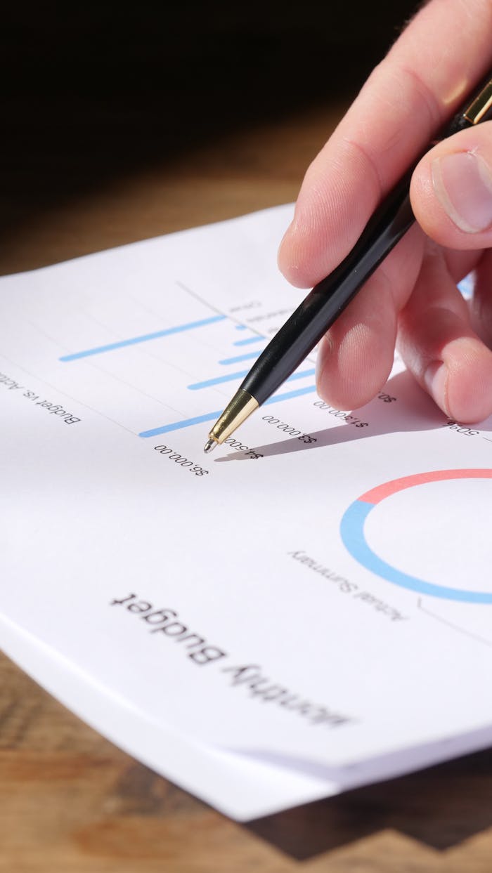 about-img Close-up of hand analyzing data on a monthly budget document with graphs and charts.